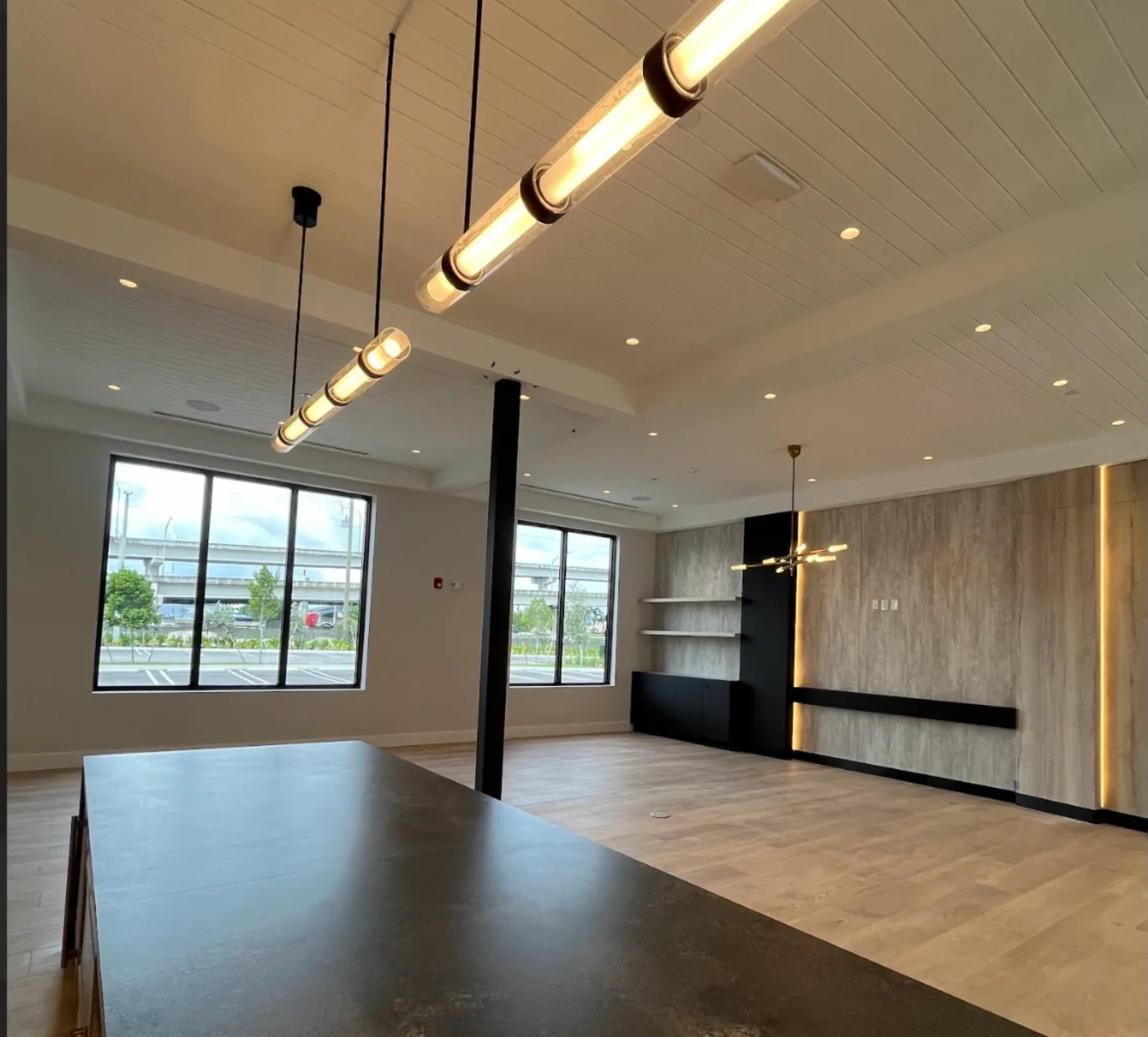 Clean clubroom with a long stone island, pendant lights and wood floors