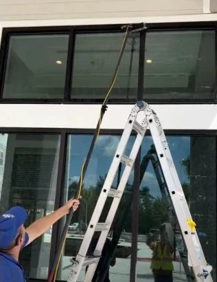 Crew member cleaning second-story glass with an extension pole